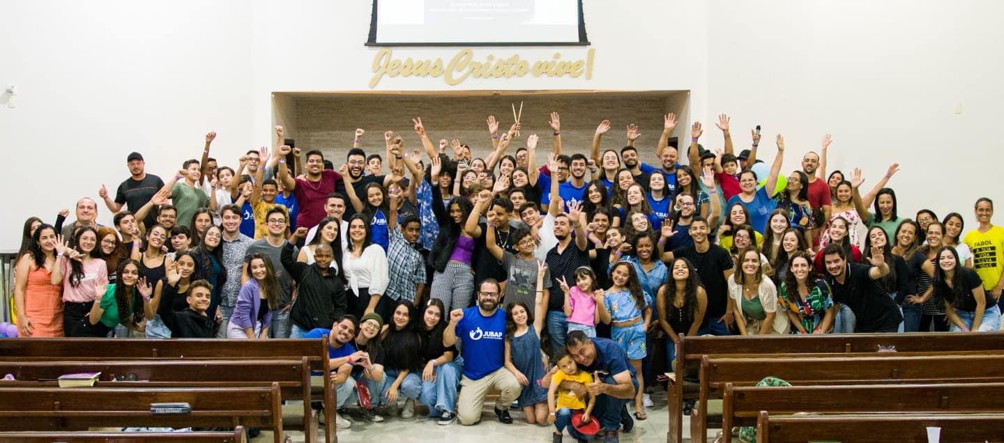 Membros da PIB Pará de Minas reunidos no templo, sorrindo e com as mãos levantadas